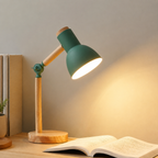 Green wooden desk lamp glowing beside books and an open page.