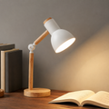 White wooden desk lamp glowing beside dark books on a walnut desk.
