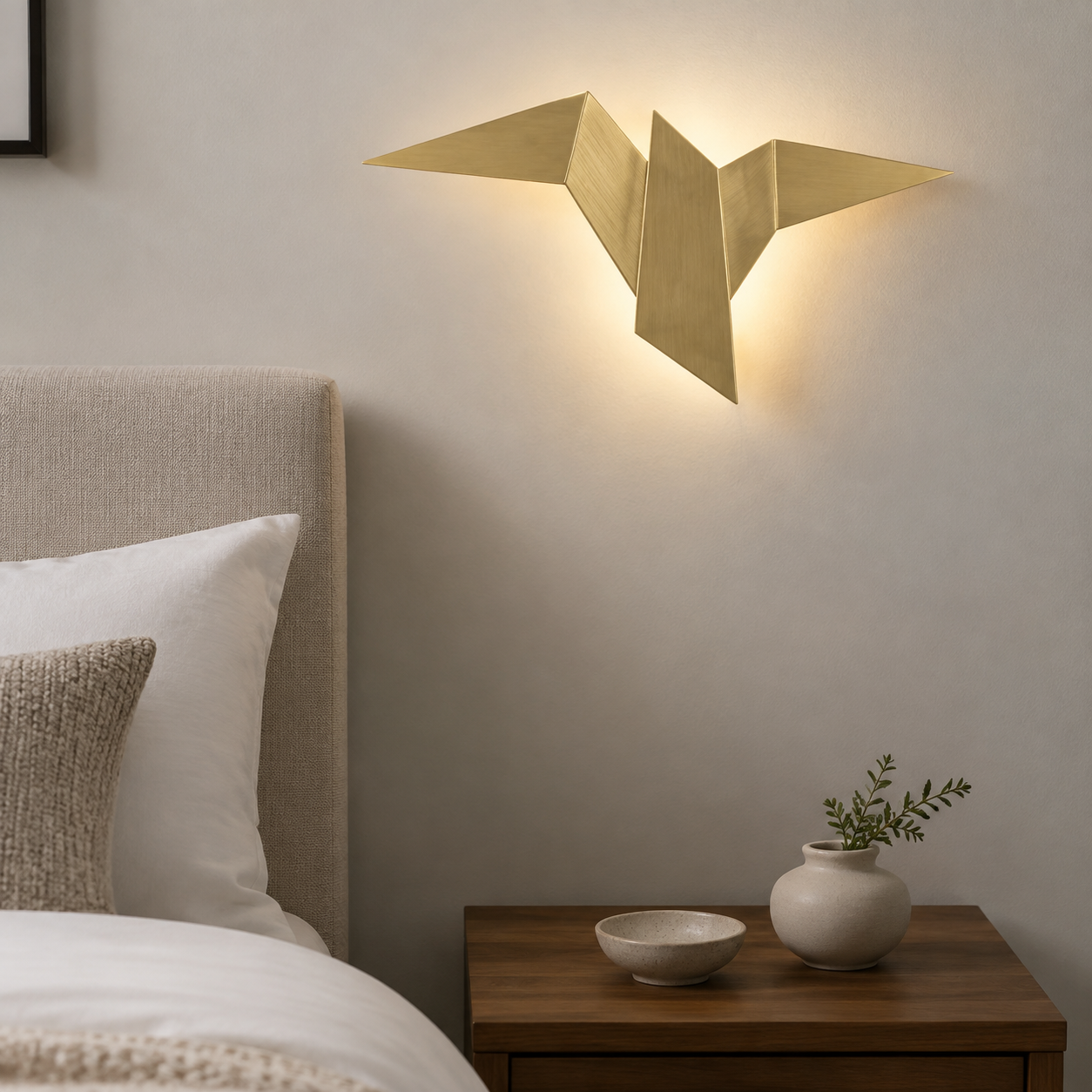 Gold origami bird LED wall sconce glowing beside an upholstered bed