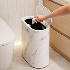 Hand placing tissue into an open cream marble oval trash can