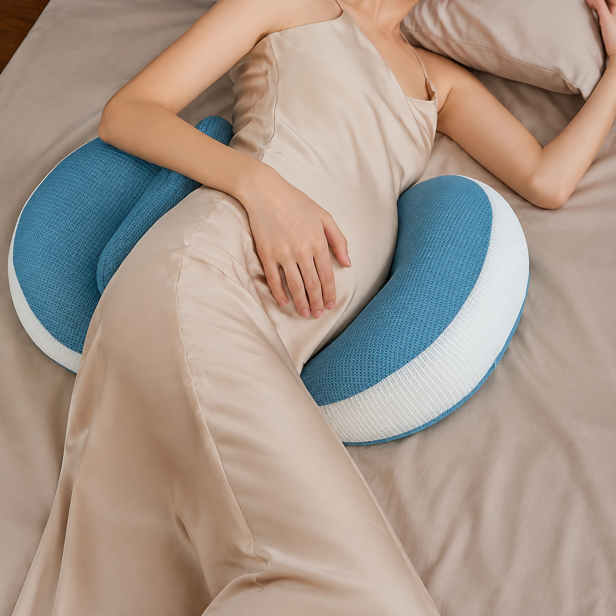 Blue pregnancy pillow positioned around a side sleeper on sand-colored bedding