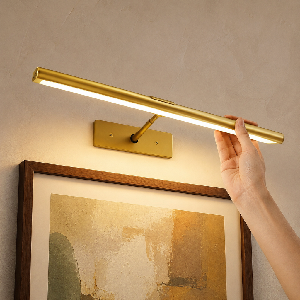 Gold rechargeable picture light adjusted by hand above framed artwork