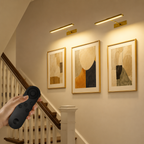 Two gold rechargeable picture lights controlled by a blank remote beside a staircase