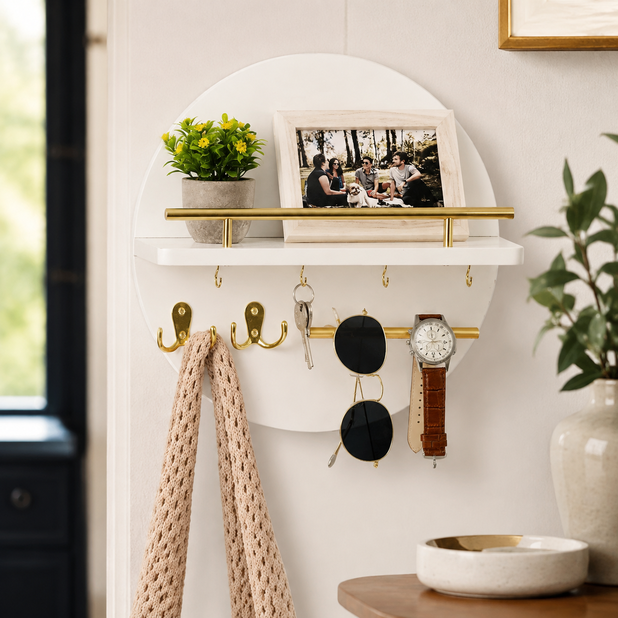 White and gold round wooden key holder styled with a plant, frame and hanging accessories.