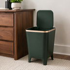 Deep green trash can with its flip-top lid open beside a walnut cabinet in a home office.