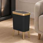 Black trash can with elevated gold legs beside a sofa in a contemporary living room.