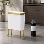 White trash can beside a bottle for scale in a minimalist studio kitchen setting.