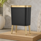 Black trash can with gold trim on a low oak studio platform.