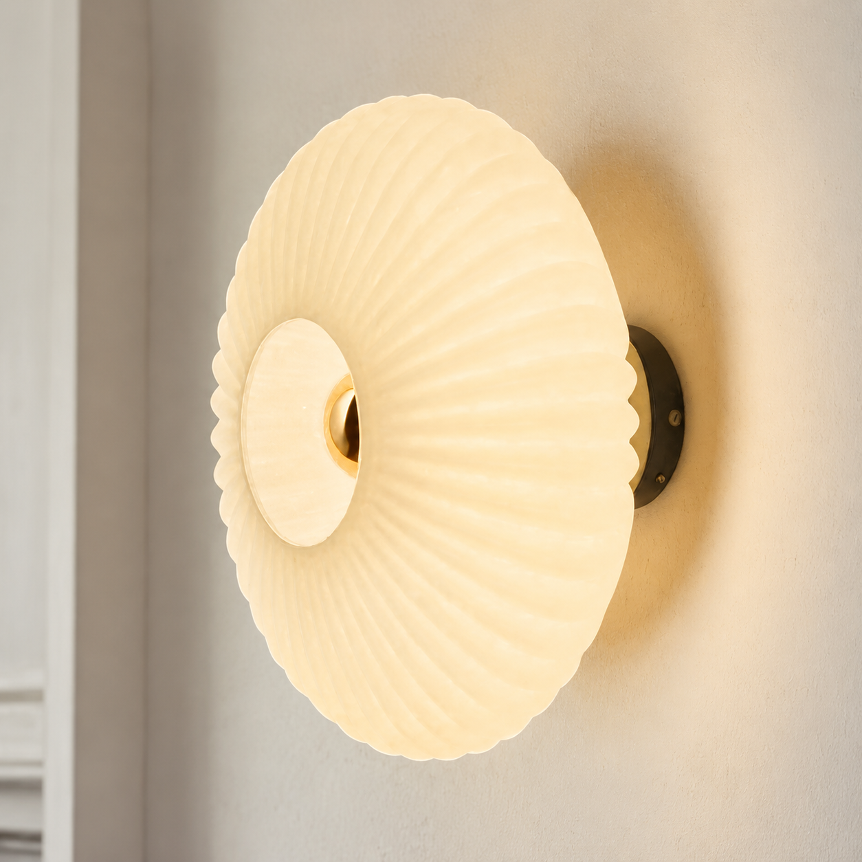 Cream ribbed glass wall sconce glowing on a warm white wall