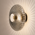 Smoked gray ribbed glass wall sconce glowing on a warm plaster wall