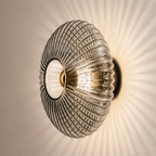 Smoked gray ribbed glass wall sconce glowing on a warm plaster wall