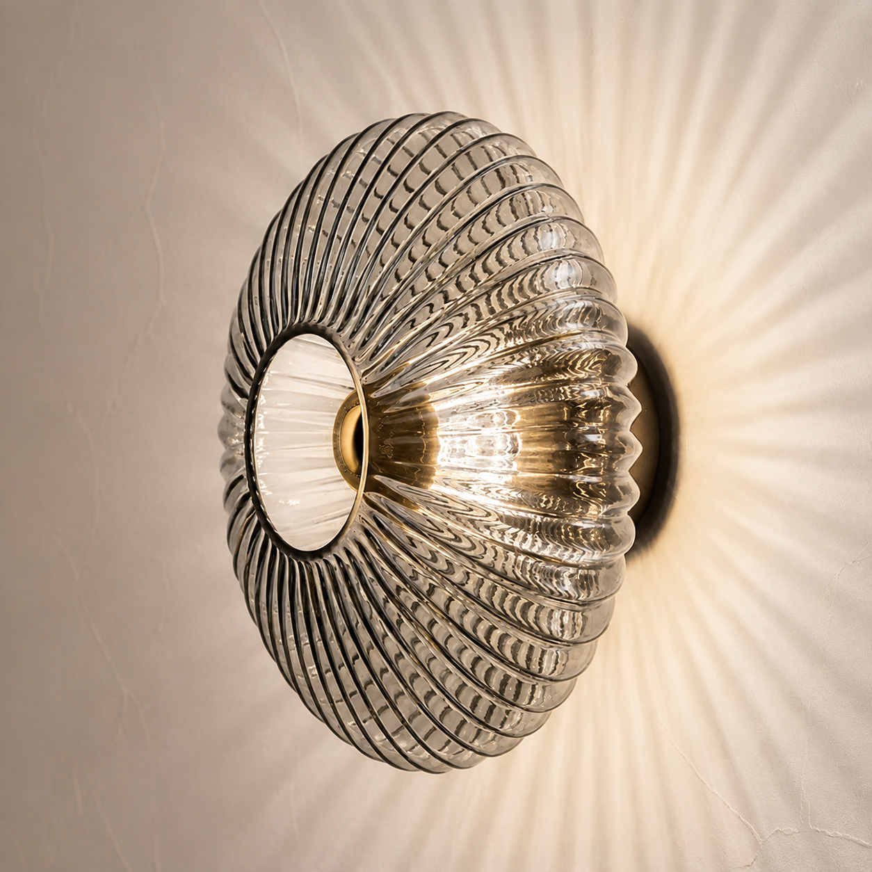 Smoked gray ribbed glass wall sconce glowing on a warm plaster wall